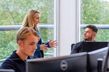 Collega’s overleggen tussen bureaus in open, groen kantoor van Bluedesk